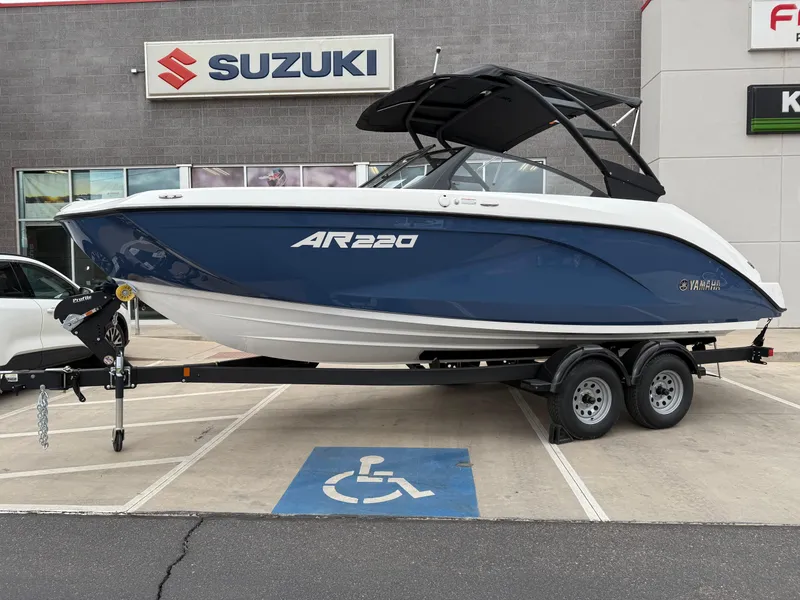 Slide: The Image of 2025 Yamaha Boats AR220 on trailer, parked in a dealership lot near Suzuki sign. - 13