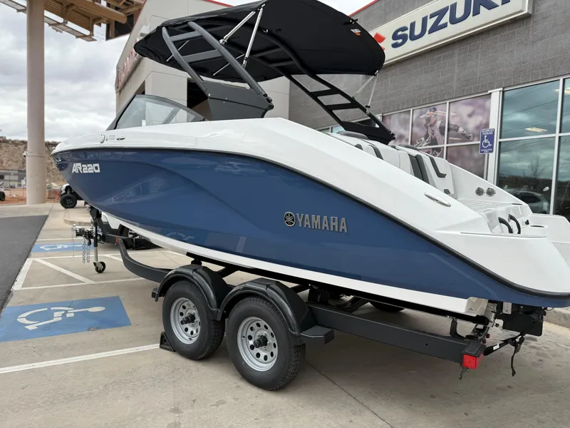 Slide: The Image of 2025 Yamaha Boats AR220 on trailer, blue and white design, parked near Suzuki dealership. - 9