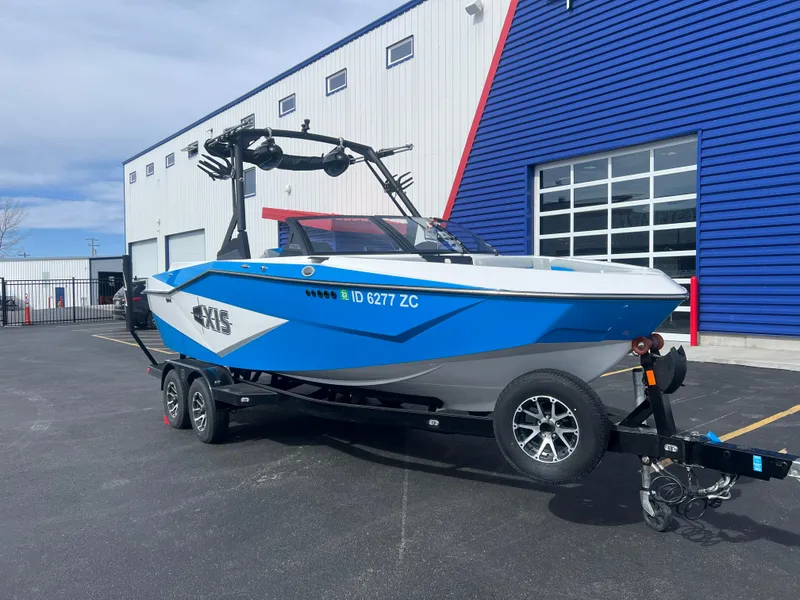 Slide: The Image of 2023 Axis Wake Research T220 boat on trailer, parked outside a blue and white building. - 3