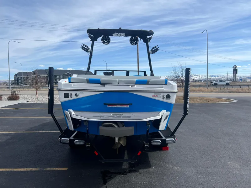 Slide: The Image of 2023 Axis Wake Research T220 boat, blue and white, parked on asphalt with mountain backdrop. - 8