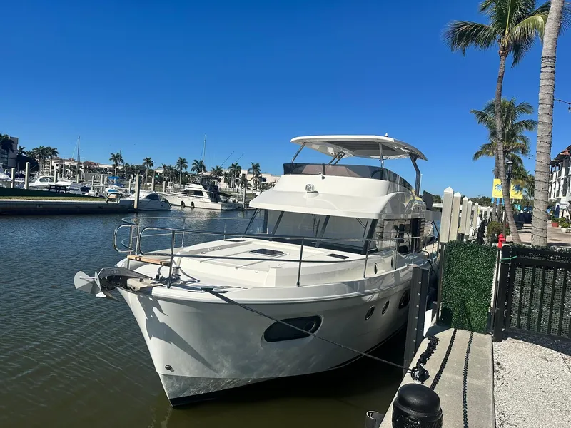 The Image of 2023 Beneteau Swift Trawler 48 docked by palm trees in a sunny marina. - 0