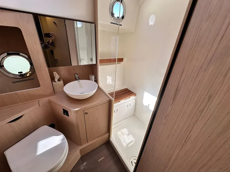 Slide: The Image of 2023 Beneteau Swift Trawler 48 bathroom with modern fixtures, wood accents, and porthole window. - 24