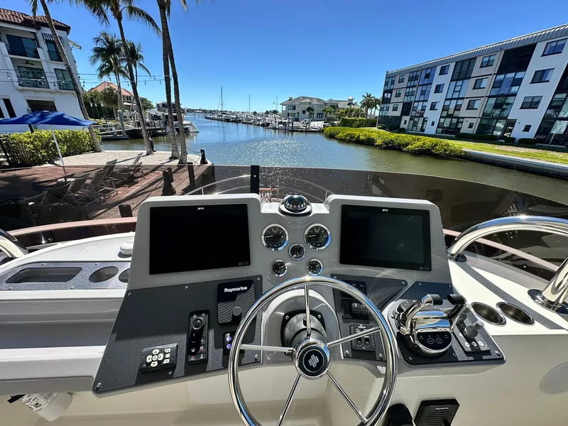 Slide: The Image of 2023 Beneteau Swift Trawler 48 helm with dual screens, docked in a sunny marina. - 26