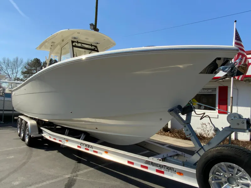 Slide: The Image of 2025 Cobia 320 Center Console boat on trailer, parked outdoors under clear blue sky. - 3