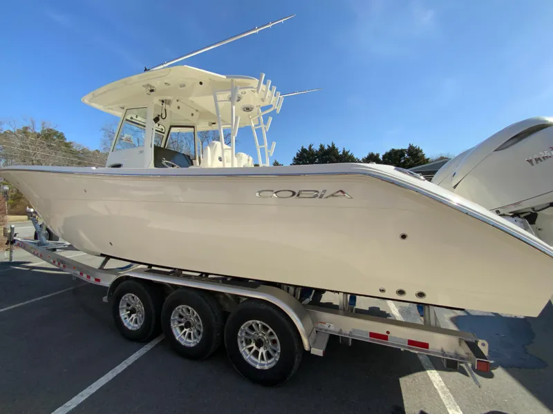 Slide: The Image of 2025 Cobia 320 Center Console boat on a trailer under clear blue sky. - 7