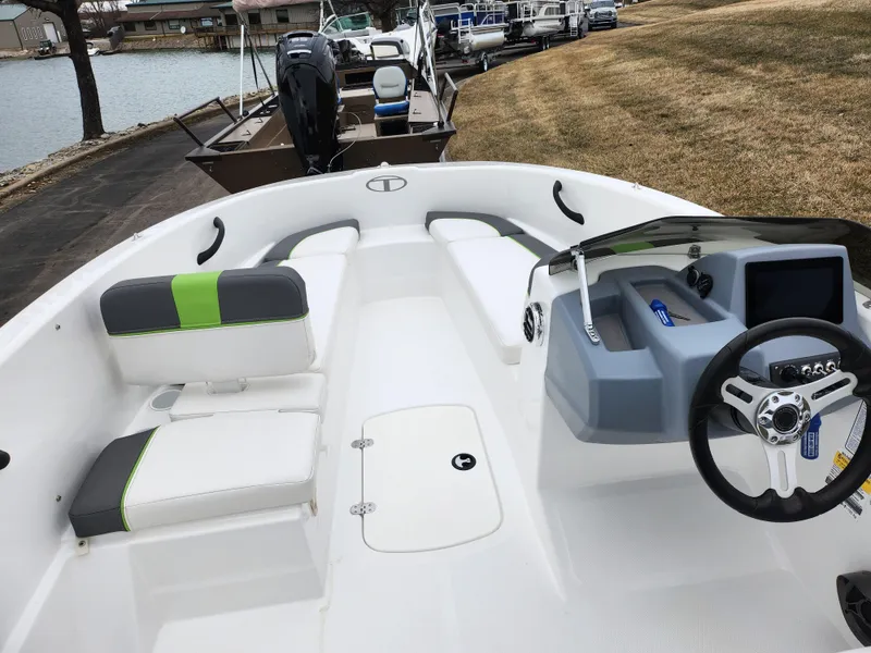 Slide: The Image of 2023 Tahoe T16 boat interior with modern seating and steering wheel, docked by a lake. - 11