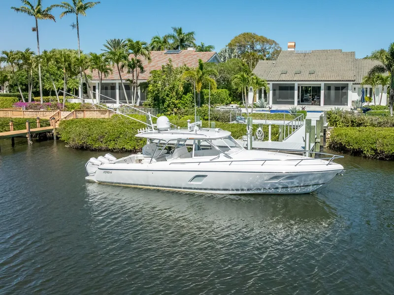 Slide: The Image of 2020 Intrepid 407 Cuddy boat docked near waterfront homes, surrounded by lush greenery. - 10