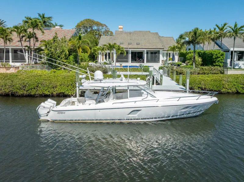 Slide: The Image of 2020 Intrepid 407 Cuddy boat docked by waterfront homes, surrounded by lush greenery. - 11
