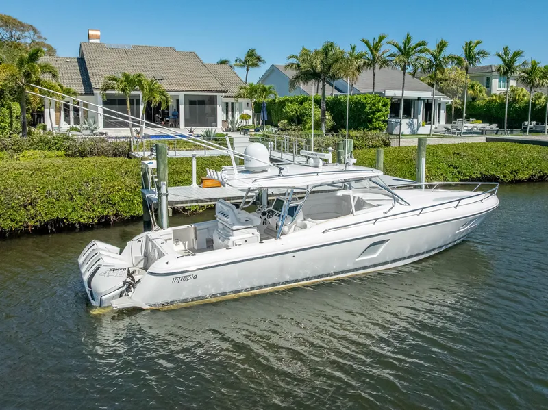 Slide: The Image of 2020 Intrepid 407 Cuddy boat docked by waterfront homes, surrounded by lush greenery. - 2