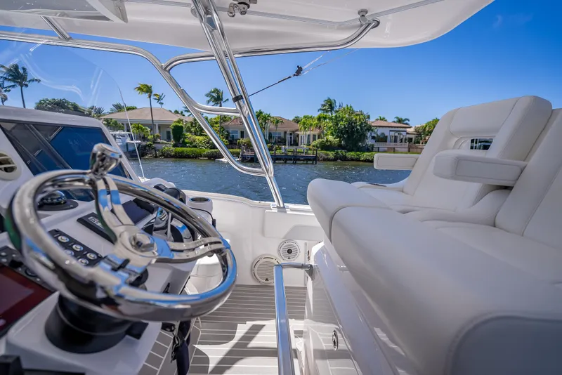 Slide: The Image of 2020 Intrepid 407 Cuddy boat interior with steering wheel and seating, overlooking waterfront homes. - 45