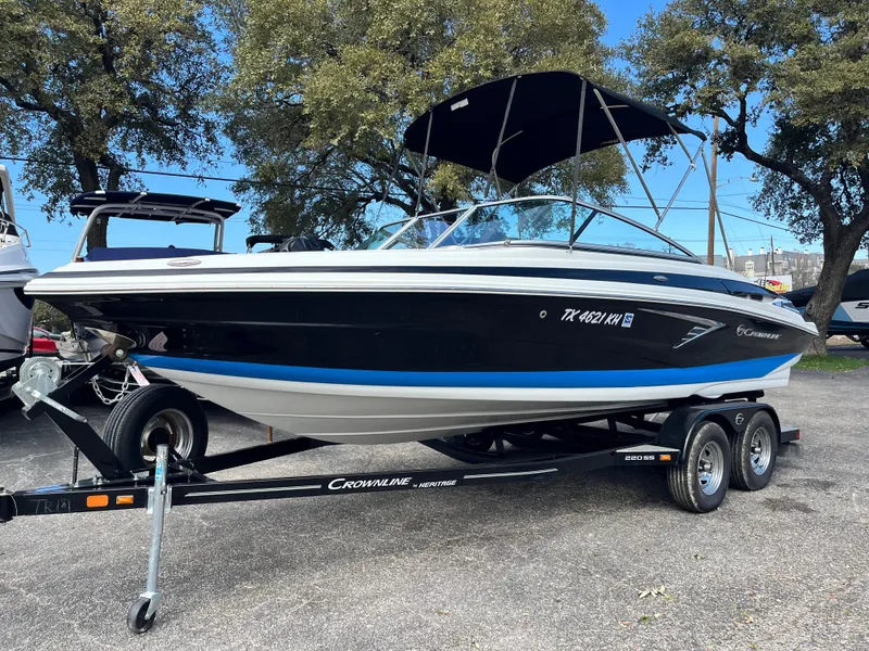 Slide: The Image of 2021 Crownline 220SS boat on trailer, parked outdoors under trees. - 3