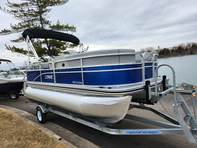 Slide: The Image of 2022 Lowe Ultra 160 Cruise pontoon boat on trailer by a lake. - 9