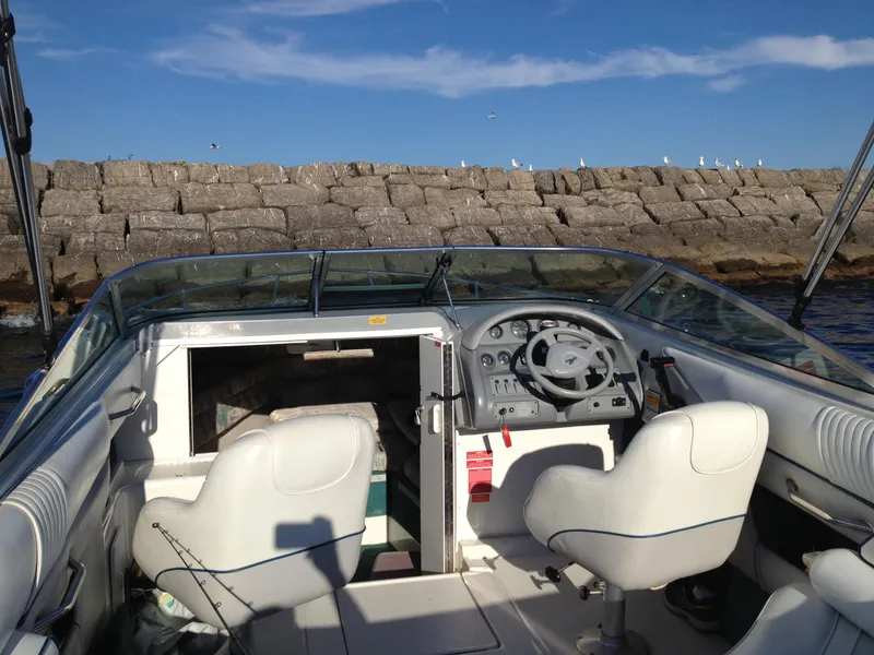 Slide: The Image of 1996 Sea Ray 240 Overnighter boat interior with steering wheel and seating, near rocky shoreline. - 4