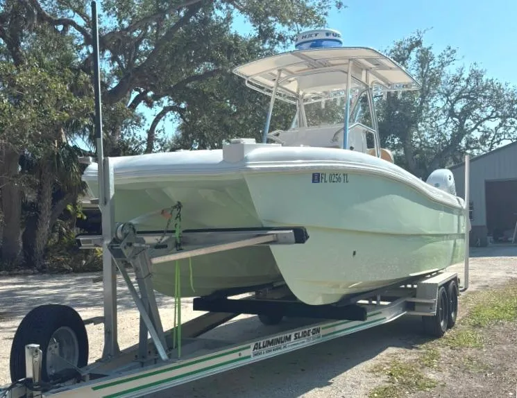 Slide: The Image of 2023 Prowler 25 boat on trailer, parked outdoors under trees. - 2