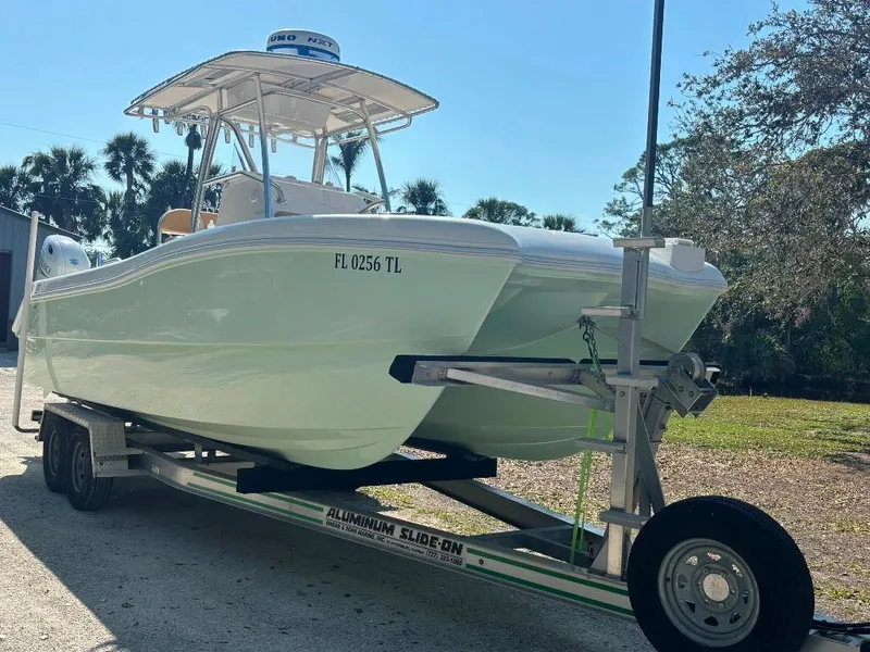 Slide: The Image of 2023 Prowler 25 boat on trailer, parked outdoors, with trees in the background. - 6