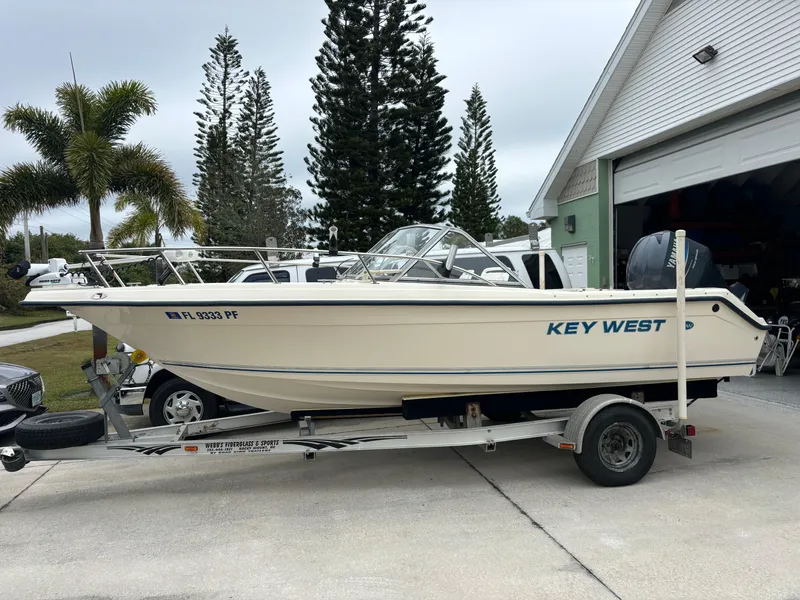 Slide: The Image of Key West 2020 Dual Console boat on trailer, parked near a garage, surrounded by trees. - 0