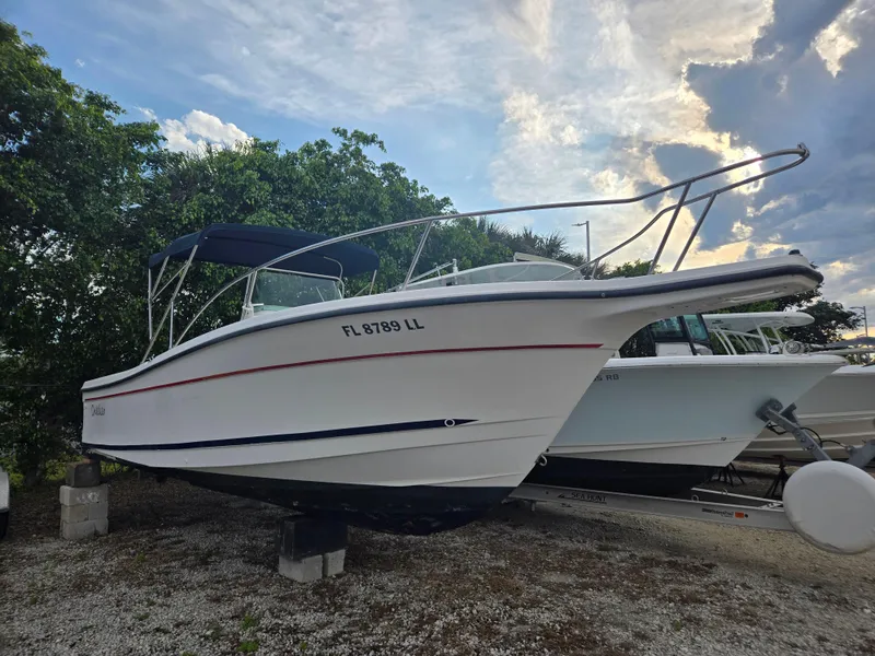 The Image of 1998 Trophy 2503 Center Console boat on dry land, under a cloudy sky. - 1