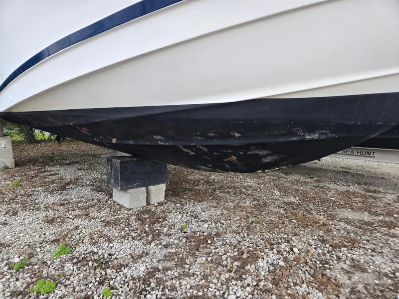 Slide: The Image of 1998 Trophy 2503 Center Console boat hull on blocks, gravel ground. - 12