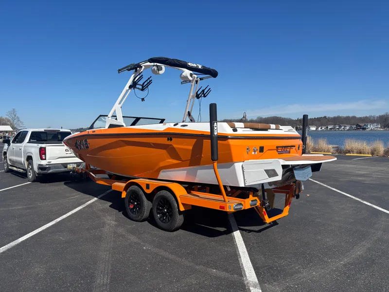 Slide: The Image of 2025 Axis A225 boat on trailer, vibrant orange, parked near a lake under clear blue sky. - 15