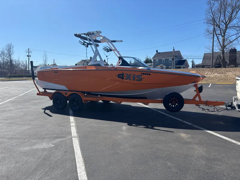 Slide: The Image of 2025 Axis A225 boat on trailer in parking lot, bright orange and white design. - 2