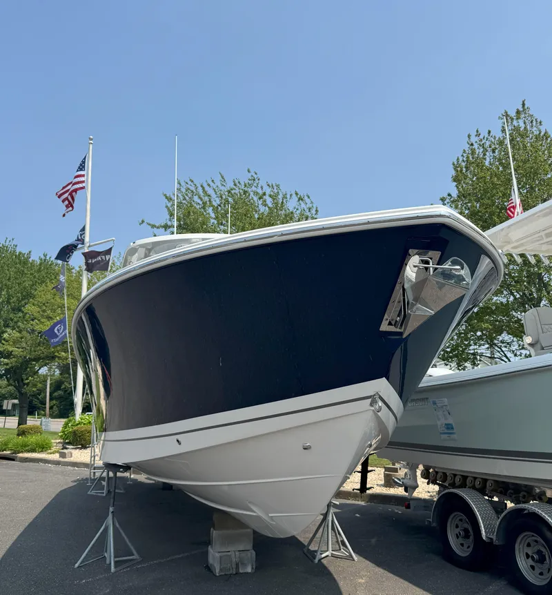 Slide: The Image of 2025 Pursuit S 328 boat displayed outdoors with flags and trees in the background. - 2