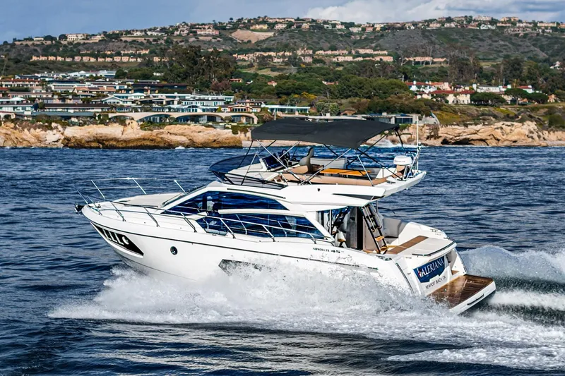 Slide: The Image of 2019 Absolute 45 FLY yacht cruising near coastal homes and rocky shoreline. - 12