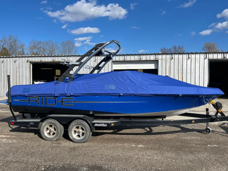 Slide: The Image of 2010 Malibu 21 vRide boat with blue cover on trailer, parked outdoors. - 1