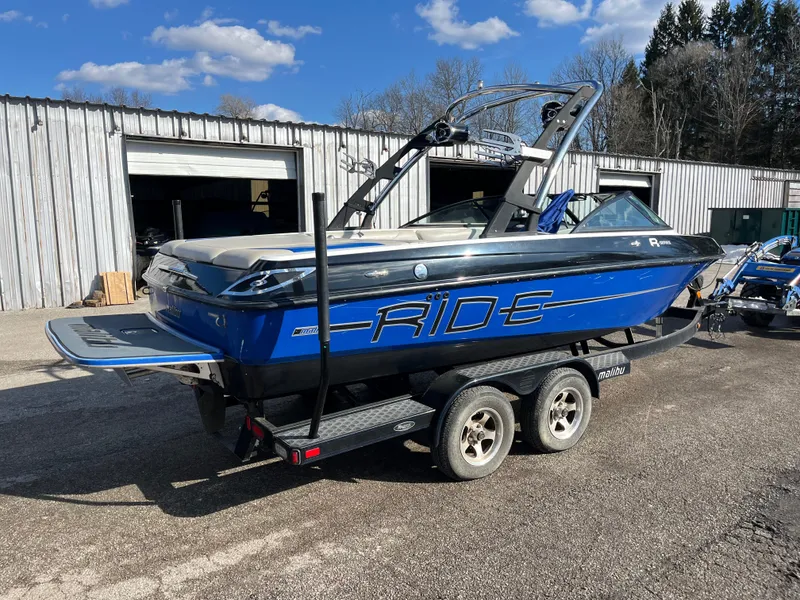 Slide: The Image of 2010 Malibu 21 vRide boat on trailer, parked outdoors near a warehouse. - 3