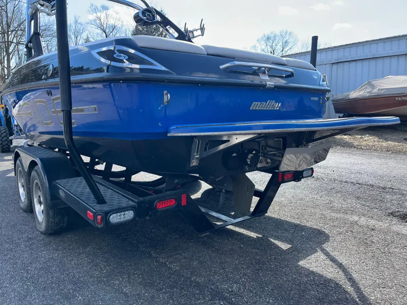 Slide: The Image of 2010 Malibu 21 vRide boat on trailer, blue and black design, parked outdoors. - 5
