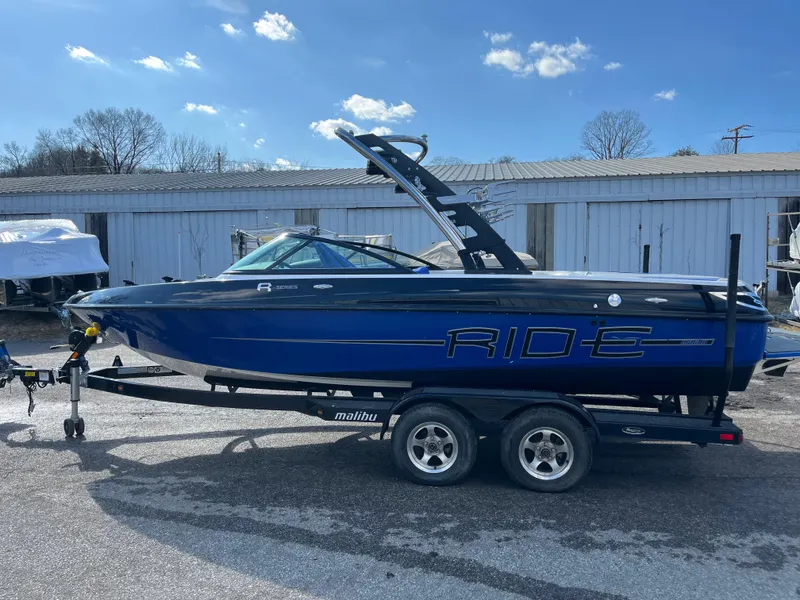 Slide: The Image of 2010 Malibu 21 vRide boat on trailer, blue and black design, parked outdoors. - 6