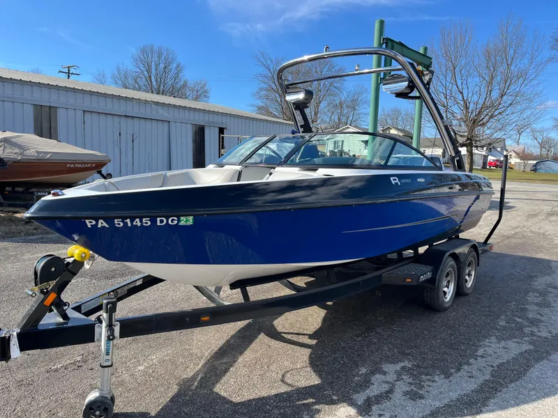 Slide: The Image of 2010 Malibu 21 vRide boat on trailer, blue and white, parked outdoors. - 7