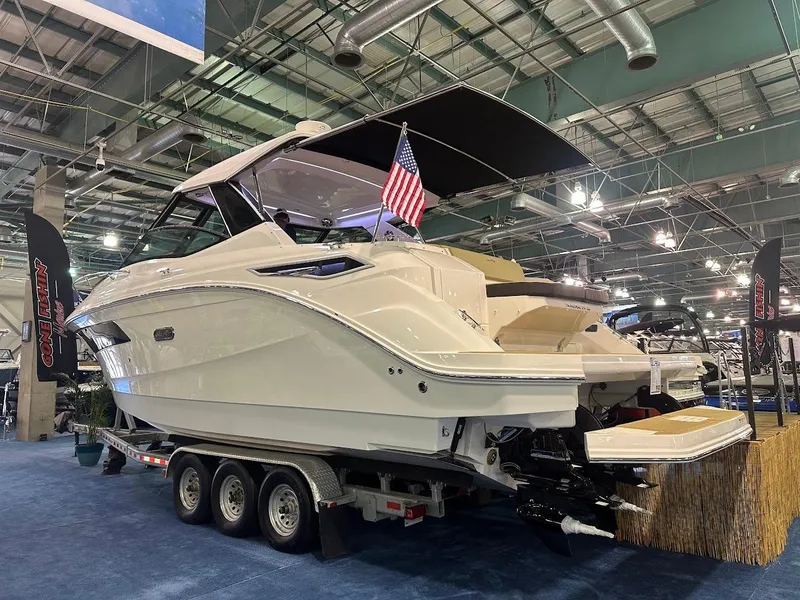 Slide: The Image of 2025 Sea Ray Sundancer 320 on display at a boat show, featuring sleek design and triple-axle trailer. - 3