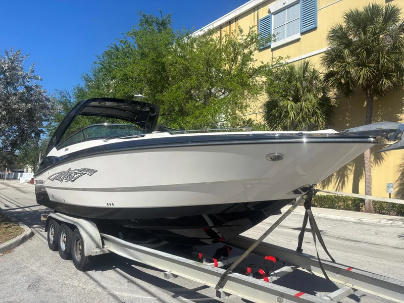 Slide: The Image of 2014 Monterey 328 Super Sport boat on trailer, parked outdoors near trees and a building. - 1