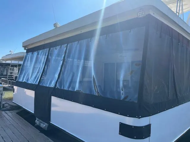 Slide: The Image of 2013 Thoroughbred houseboat with clear vinyl enclosures docked under bright sunlight. - 2