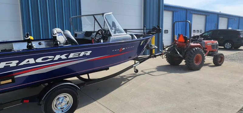 Slide: The Image of 2016 Tracker Pro Guide V-16 WT boat hitched to a tractor outside blue storage units. - 2
