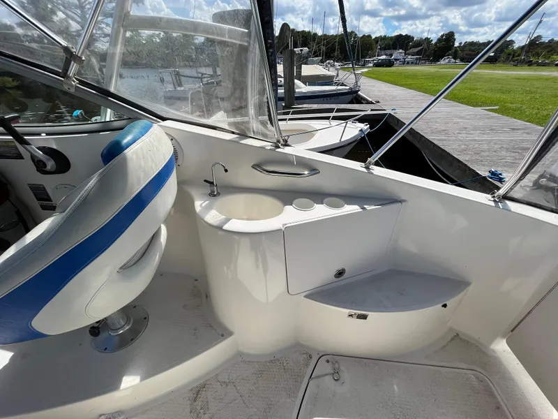 Slide: The Image of 2006 Bayliner 265 Cruiser interior with helm seat and sink, docked by grassy shore. - 16
