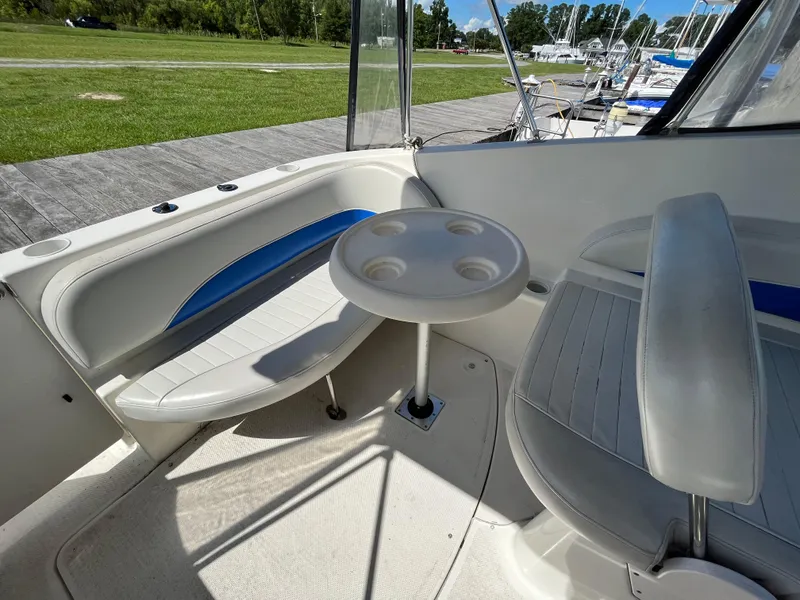 Slide: The Image of 2006 Bayliner 265 Cruiser interior with seating and table, docked near green lawn. - 17