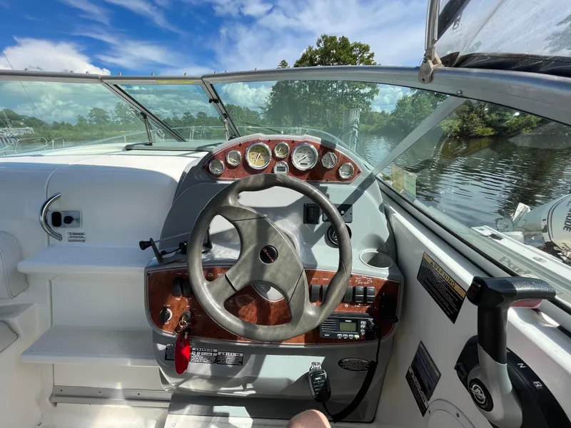 Slide: The Image of 2006 Bayliner 265 Cruiser helm with gauges, steering wheel, and scenic waterway view. - 18