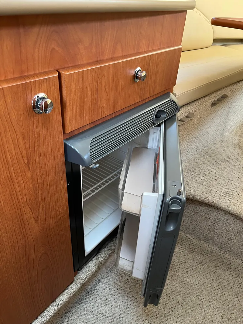 Slide: The Image of Open mini fridge in 2006 Bayliner 265 Cruiser, wooden cabinetry, beige carpet. - 24