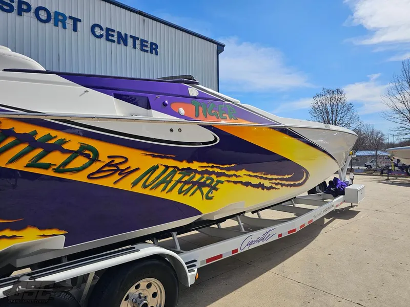 Slide: The Image of 2003 Cigarette 42 Tiger boat with vibrant graphics on a trailer outside a sports center. - 11