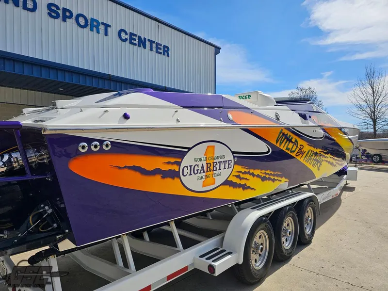 Slide: The Image of 2003 Cigarette 42 Tiger boat with vibrant graphics on a trailer outside a sports center. - 8