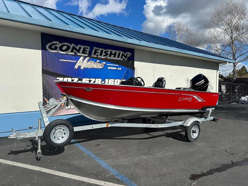 Slide: The Image of 2025 Lund 1400 Fury SS boat in red on a trailer, parked outside a dealership. - 1
