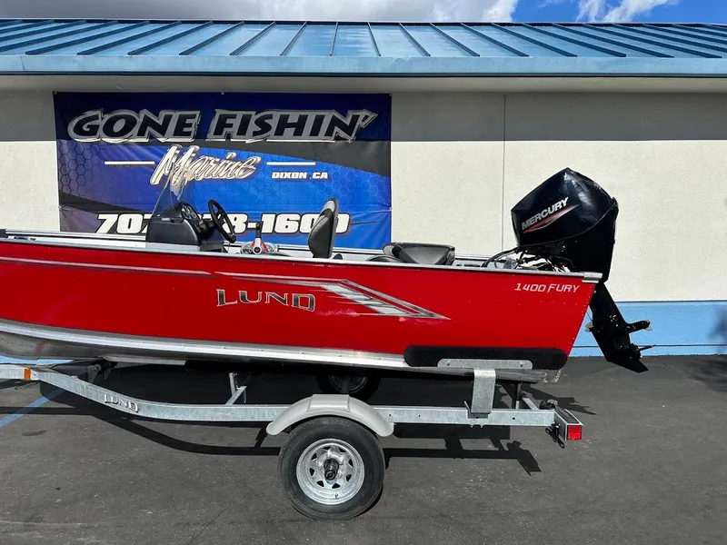 Slide: The Image of 2025 Lund 1400 Fury SS boat on trailer, red exterior, Mercury outboard motor, parked outside. - 5