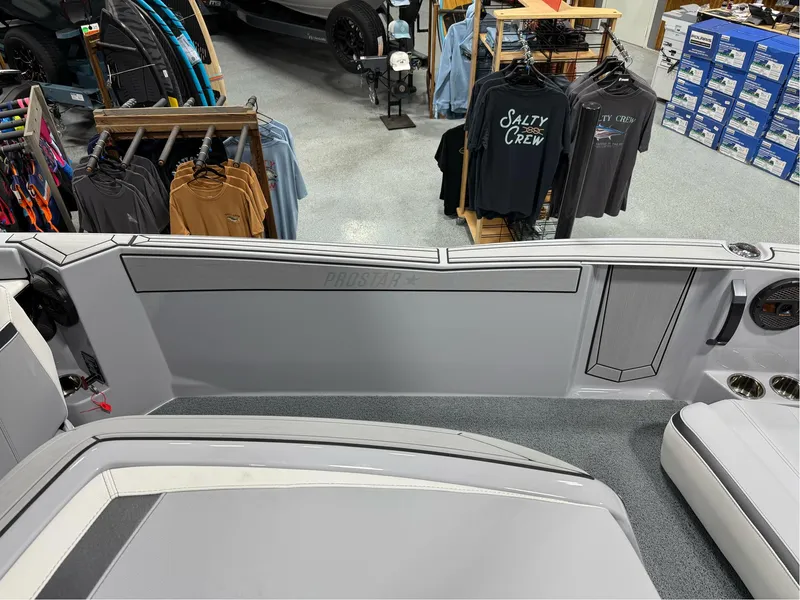 Slide: The Image of 2025 MasterCraft ProStar interior with gray seating, displayed in a showroom with clothing racks. - 20
