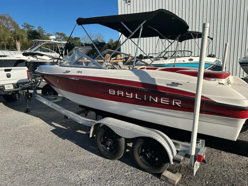 Slide: The Image of 2012 Bayliner 185 Bowrider boat on trailer, parked outdoors near other boats. - 2