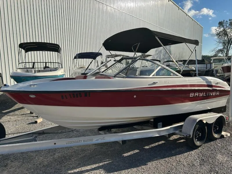 Slide: The Image of 2012 Bayliner 185 Bowrider boat on trailer, red and white, with canopy, parked outdoors. - 3