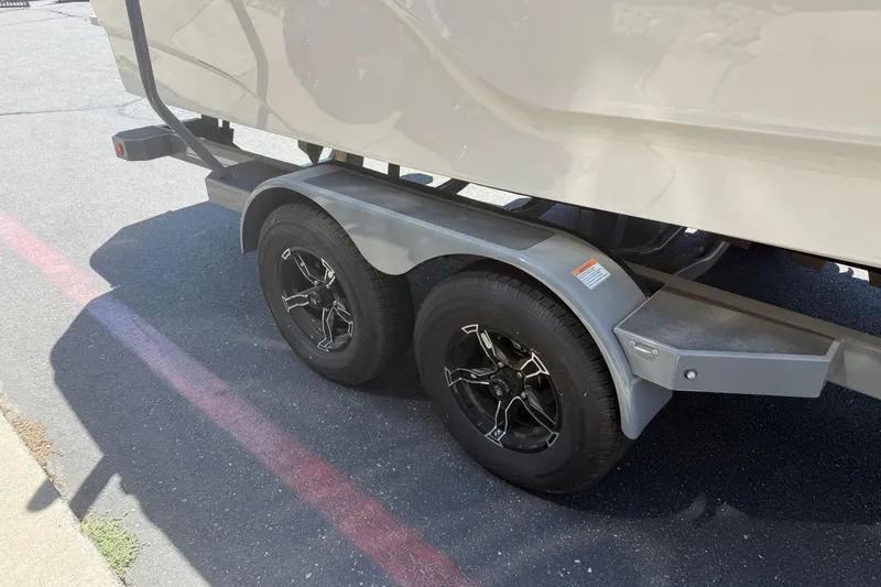 Slide: The Image of 2025 MasterCraft XT24 boat trailer with dual black wheels on asphalt. - 12
