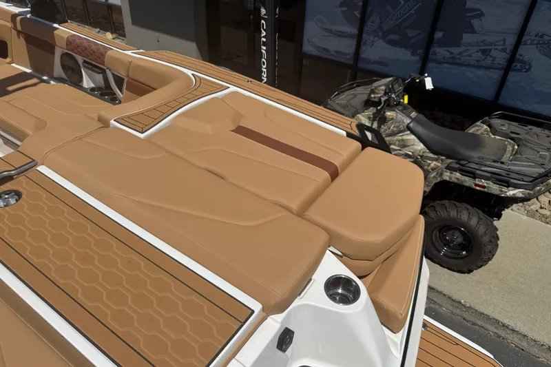 Slide: The Image of 2025 MasterCraft XT24 boat with tan seating and cup holders, parked beside an ATV. - 15