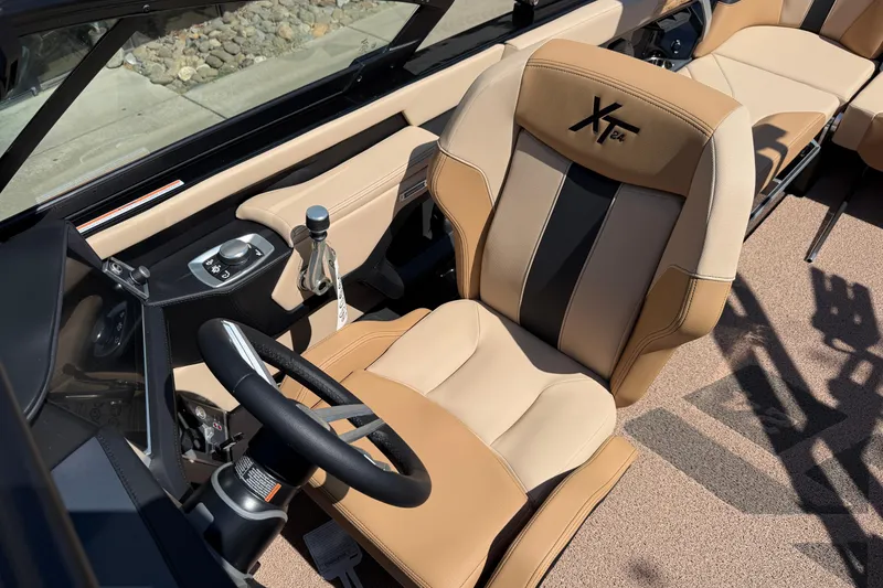 Slide: The Image of 2025 MasterCraft XT24 boat interior with tan and black seating, steering wheel, and controls. - 23