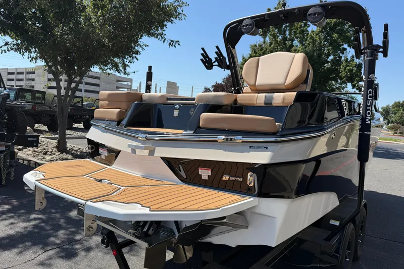 Slide: The Image of 2025 MasterCraft XT24 boat with tan seating and teak swim platform, parked outdoors. - 7